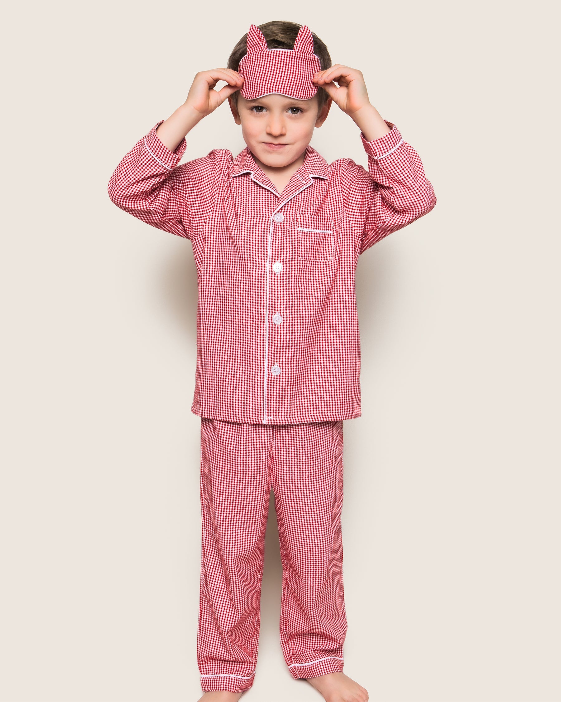 Child wearing red checkered pajama set with matching headband on a beige background