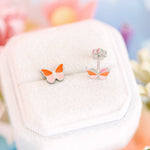 Butterfly-shaped earrings on a white cushion with a colorful blurred background