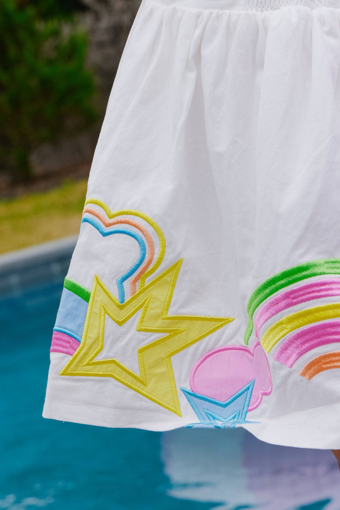 White dress close up with colorful designs of rainbows and stars on a poolside background