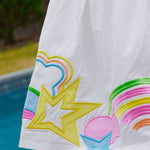 White dress close up with colorful designs of rainbows and stars on a poolside background