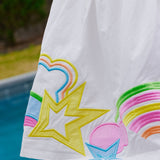 White dress close up with colorful designs of rainbows and stars on a poolside background