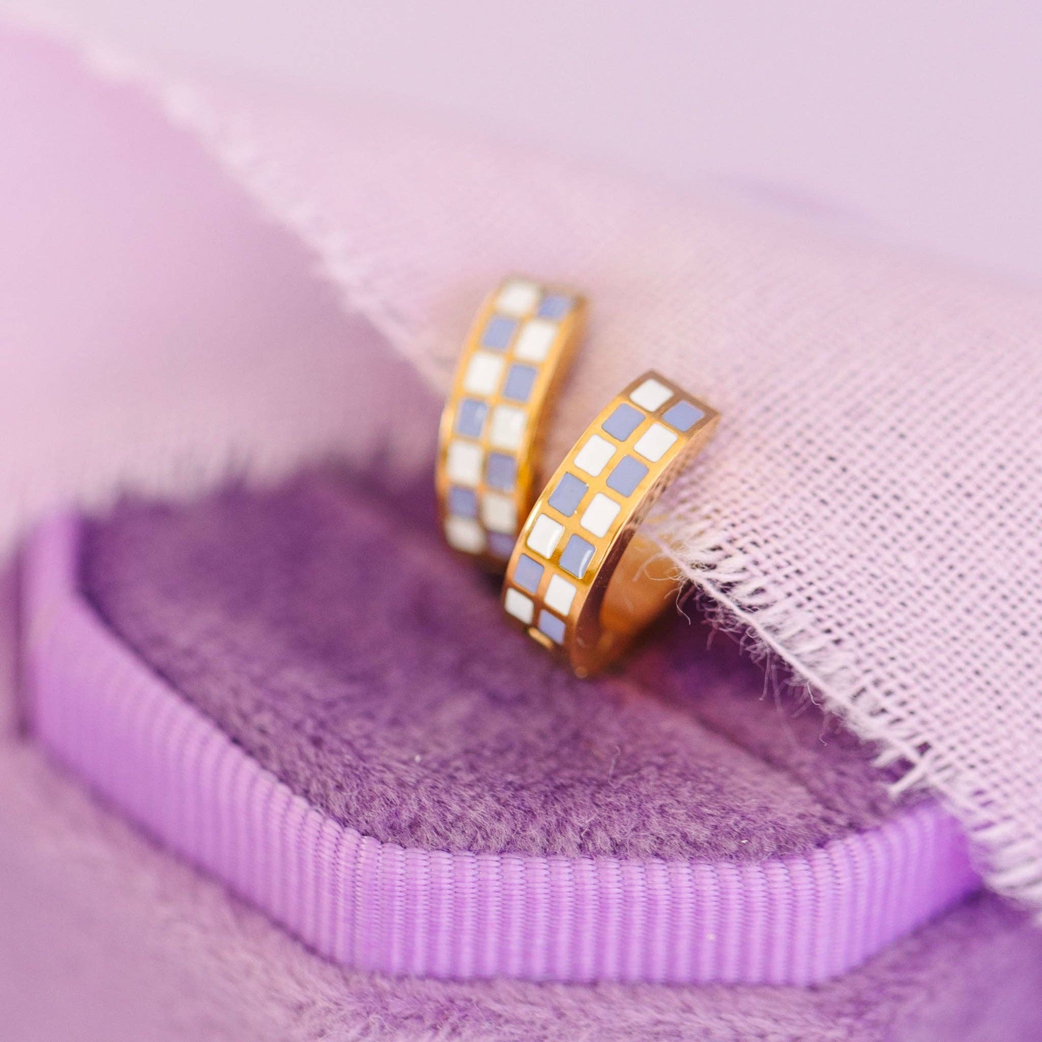 Two gold hoop earrings with a checkered purple white pattern on a purple fabric background