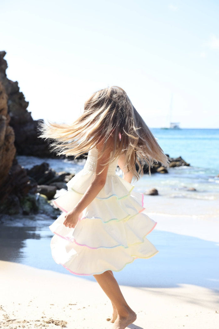 girl in a white tiered dress with long hair standing on a beach.