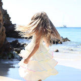 girl in a white tiered dress with long hair standing on a beach.