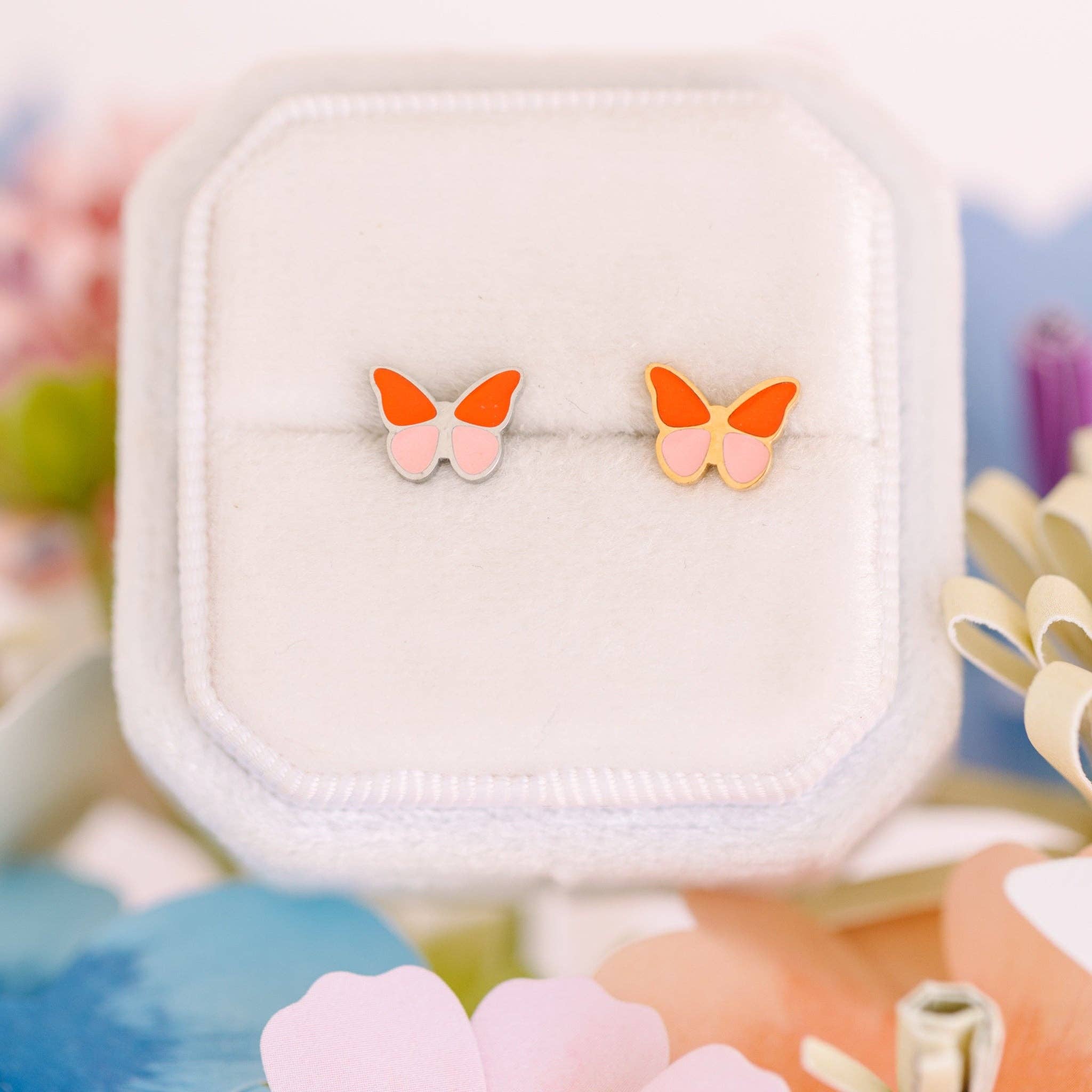 Butterfly-shaped earrings on a white stand with a colorful background