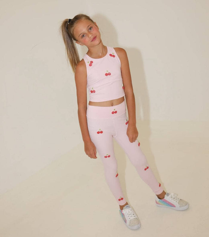Young girl wearing a pink outfit with cherry patterns on a plain background