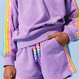 Person wearing a purple outfit with rainbow trim on a light blue background
