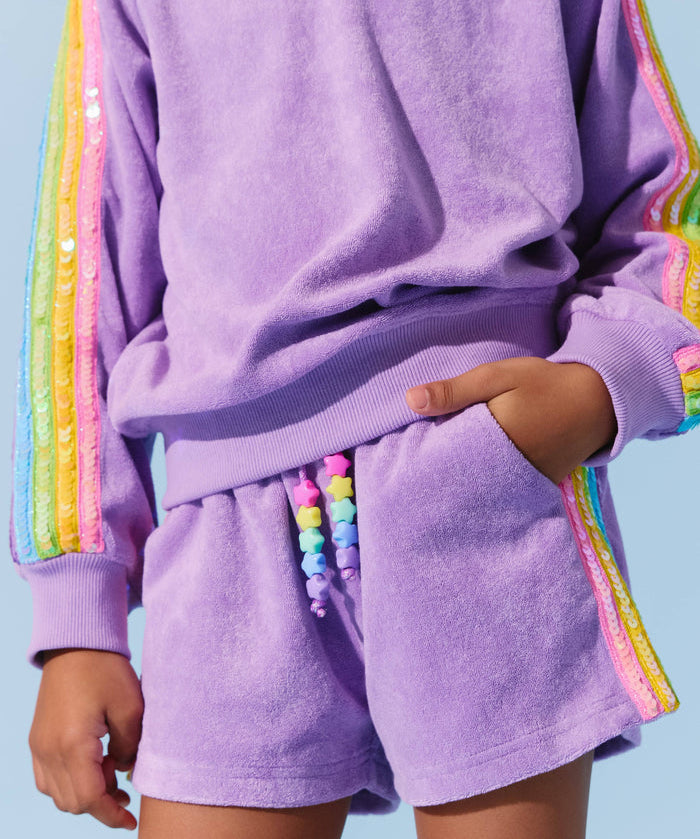 Person wearing a purple outfit with rainbow trim on a light blue background