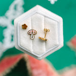 winter mushroom earrings in a hexagonal white jewelry box on a green background