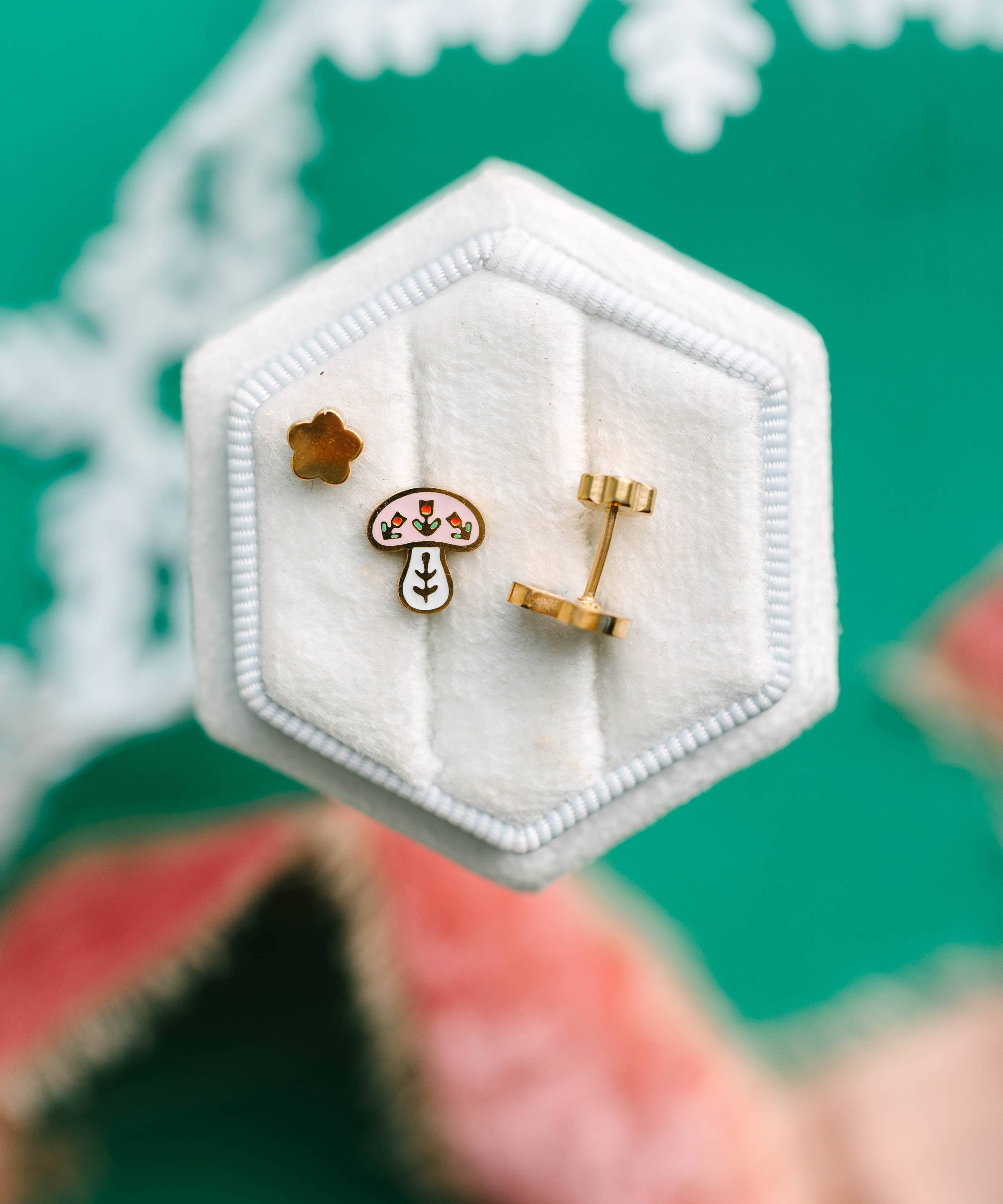 winter mushroom earrings in a hexagonal white jewelry box on a green background