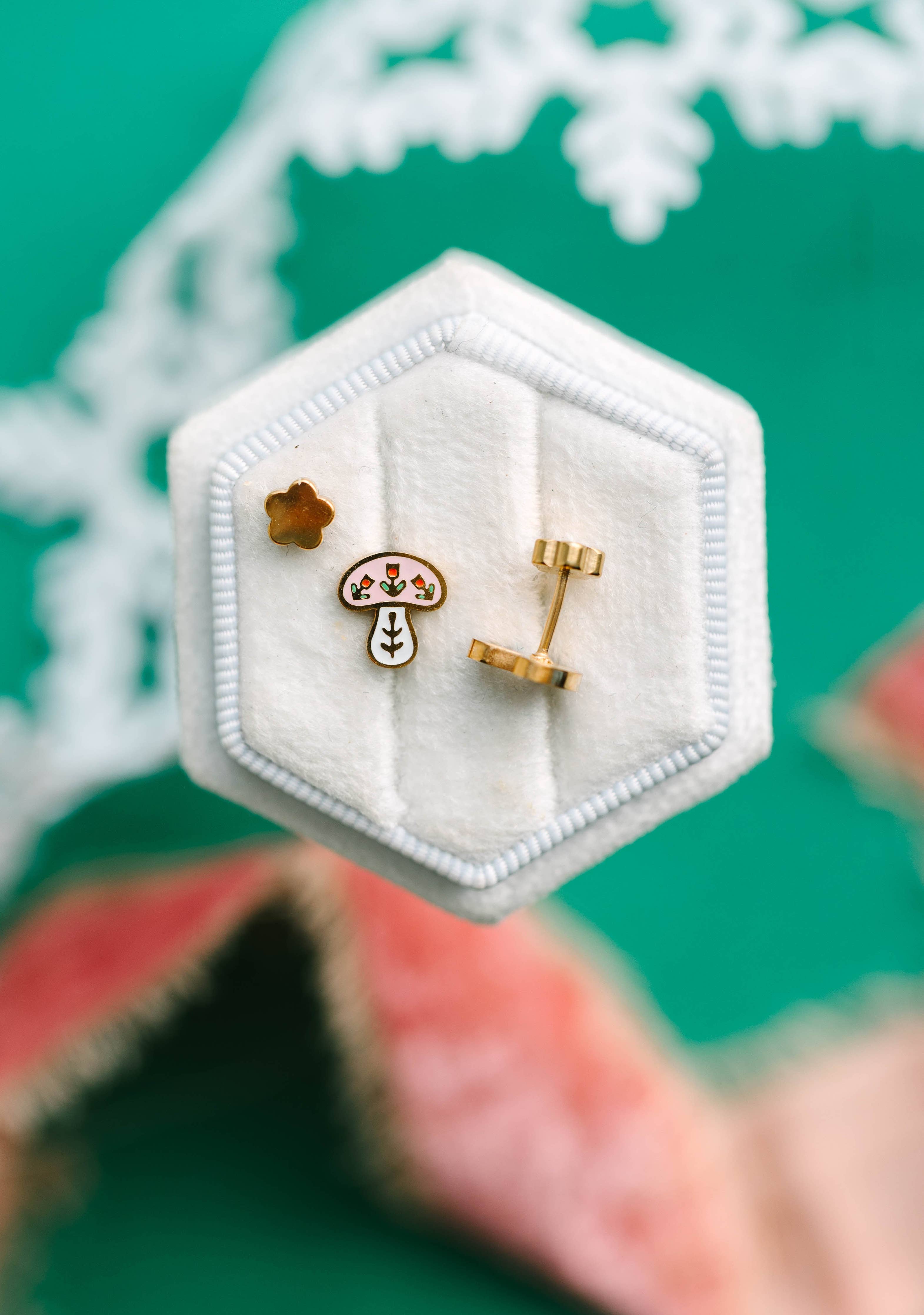 winter mushroom earrings in a hexagonal white jewelry box on a green background