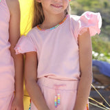 Two young girls in matching pink outfits with rainbow accents standing on a beach.