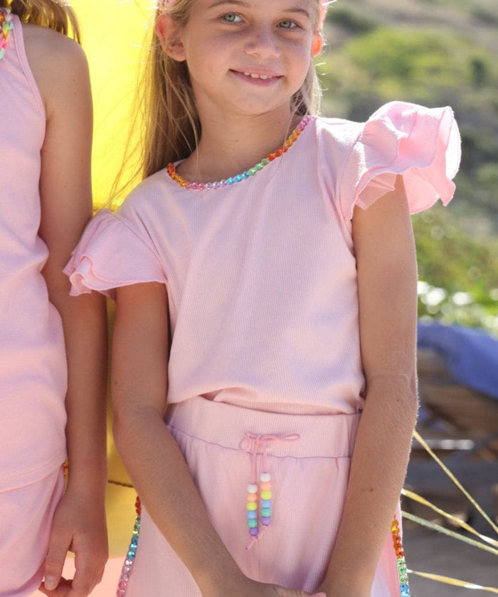 Two young girls in matching pink outfits with rainbow accents standing on a beach.