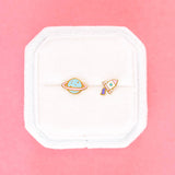 space earrings, one planet and one rocket ship on a cushion with prink background