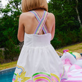 girl wearing a white dress with colorful designs by a poolside.