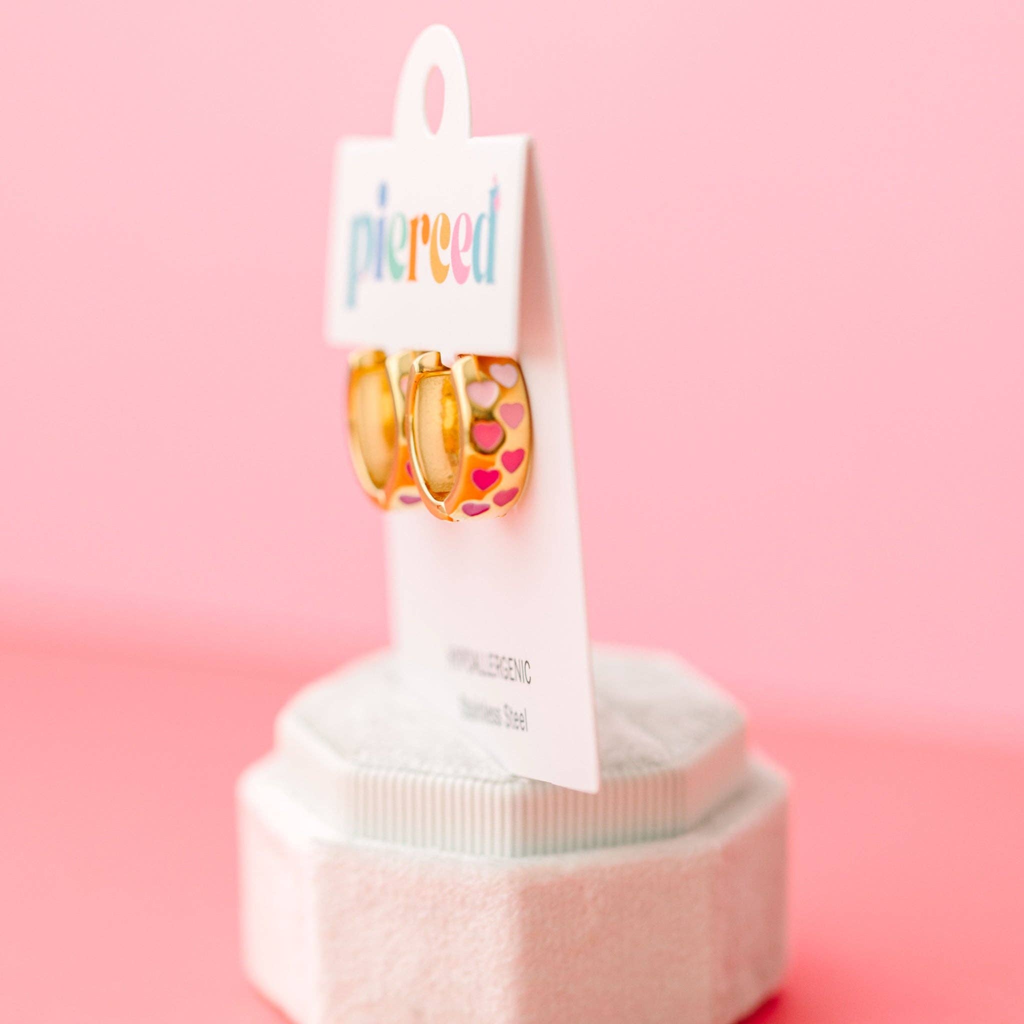Pair of pink ombre heart print hoop earrings on a 'pierced' branded card against a pink background
