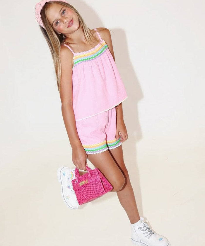 Young girl in a pink outfit with colorful accents holding a pink bag on a white background