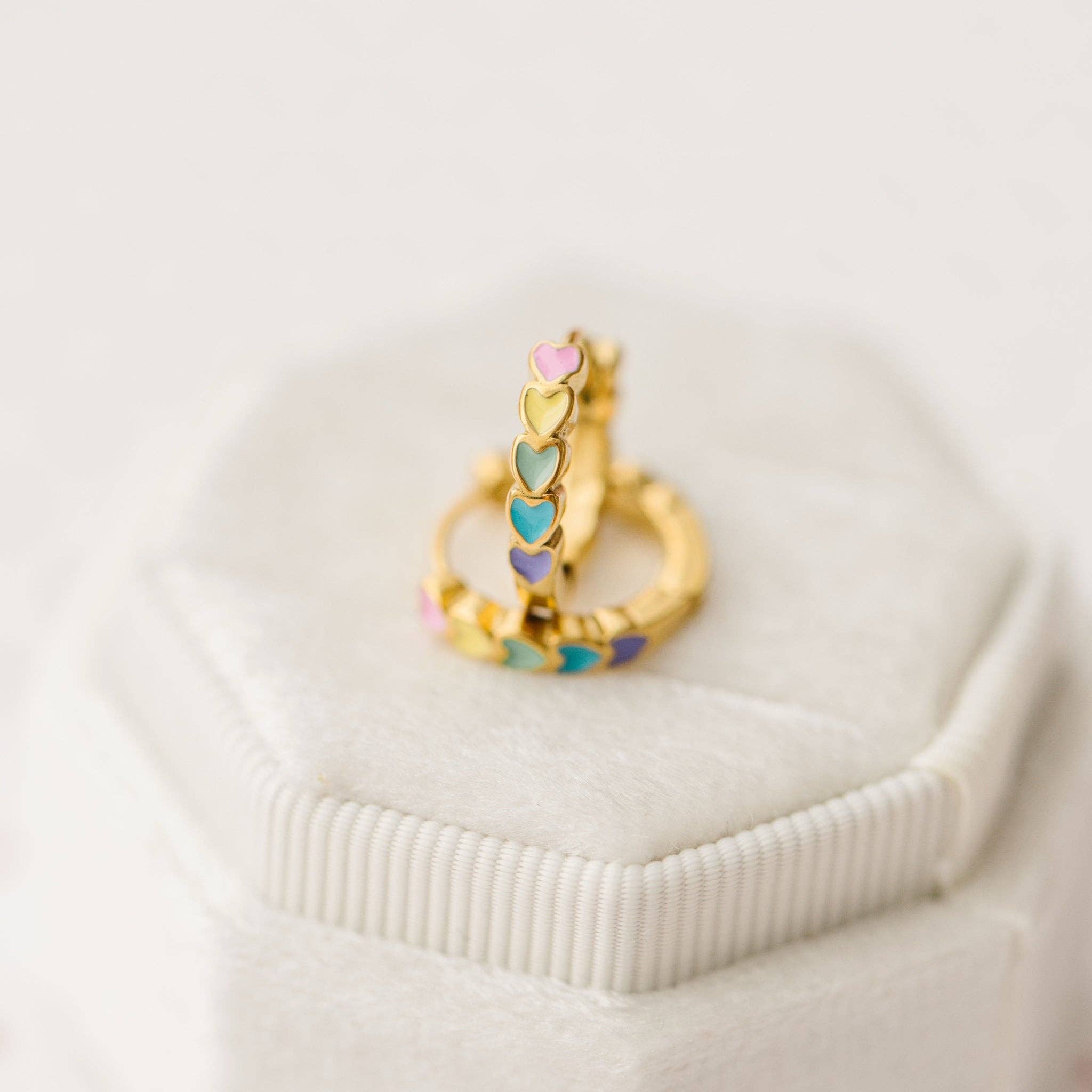Gold earrings with colorful rainbow heart-shaped stones on a white background