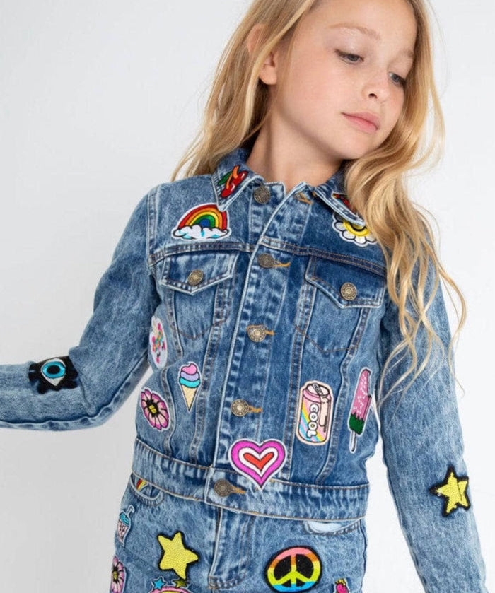 Child wearing a denim jacket with colorful patches on a white background