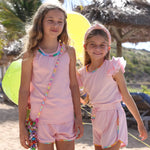 Two young girls in matching pink outfits standing on a sandy beach with palm trees 