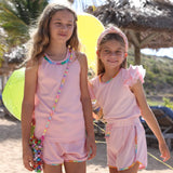 Two young girls in matching pink outfits standing on a sandy beach with palm trees 
