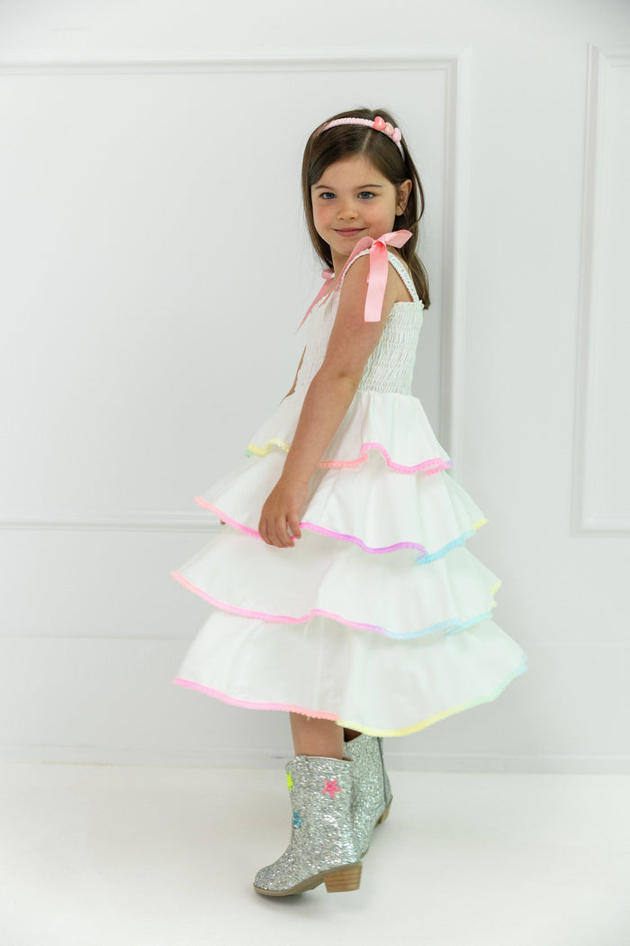 Young girl wearing a white dress with colorful trim and sparkly boots on a white background