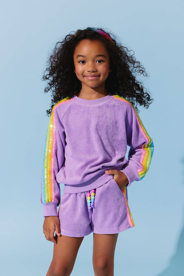 Child wearing a purple outfit with rainbow sleeves against a light blue background
