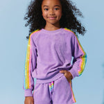 Child wearing a purple outfit with rainbow sleeves against a light blue background