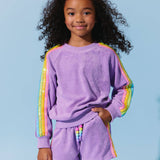 Child wearing a purple outfit with rainbow sleeves against a light blue background