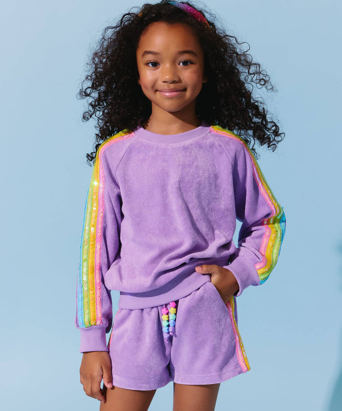 Child wearing a purple outfit with rainbow sleeves against a light blue background