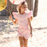 Young girl in a pink outfit with gem trim holding balloons on a sandy beach.