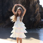 Young girl in a white dress standing on a beach with large rocks in the background