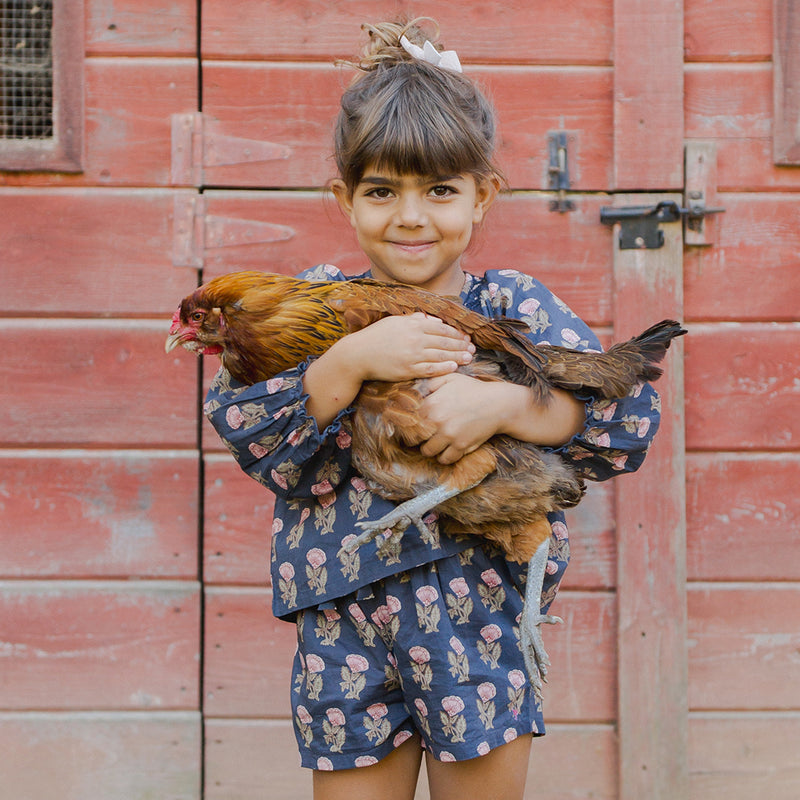 girl wearing navy floral shorts holding a chicken 