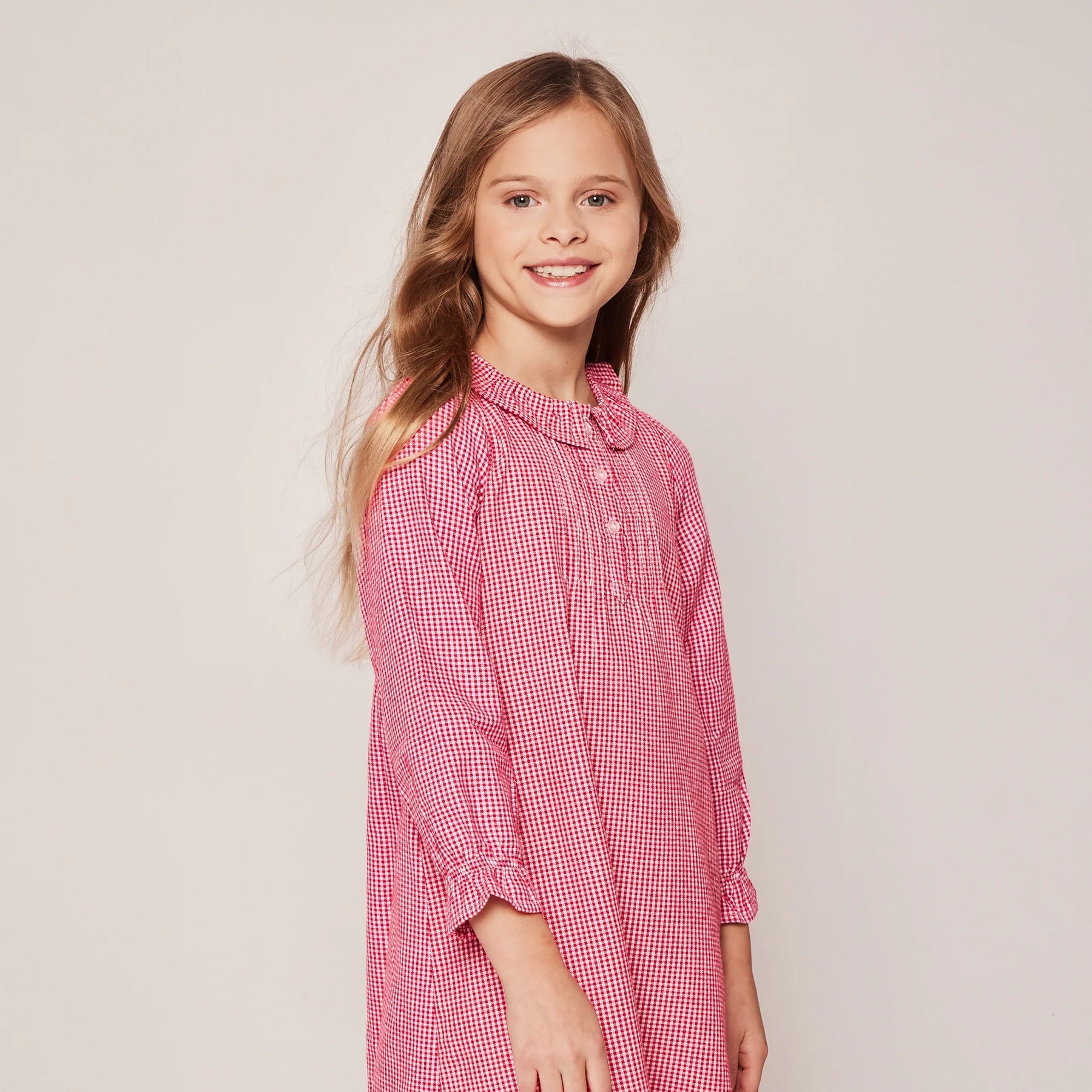 Young girl wearing a red checkered dress against a plain background