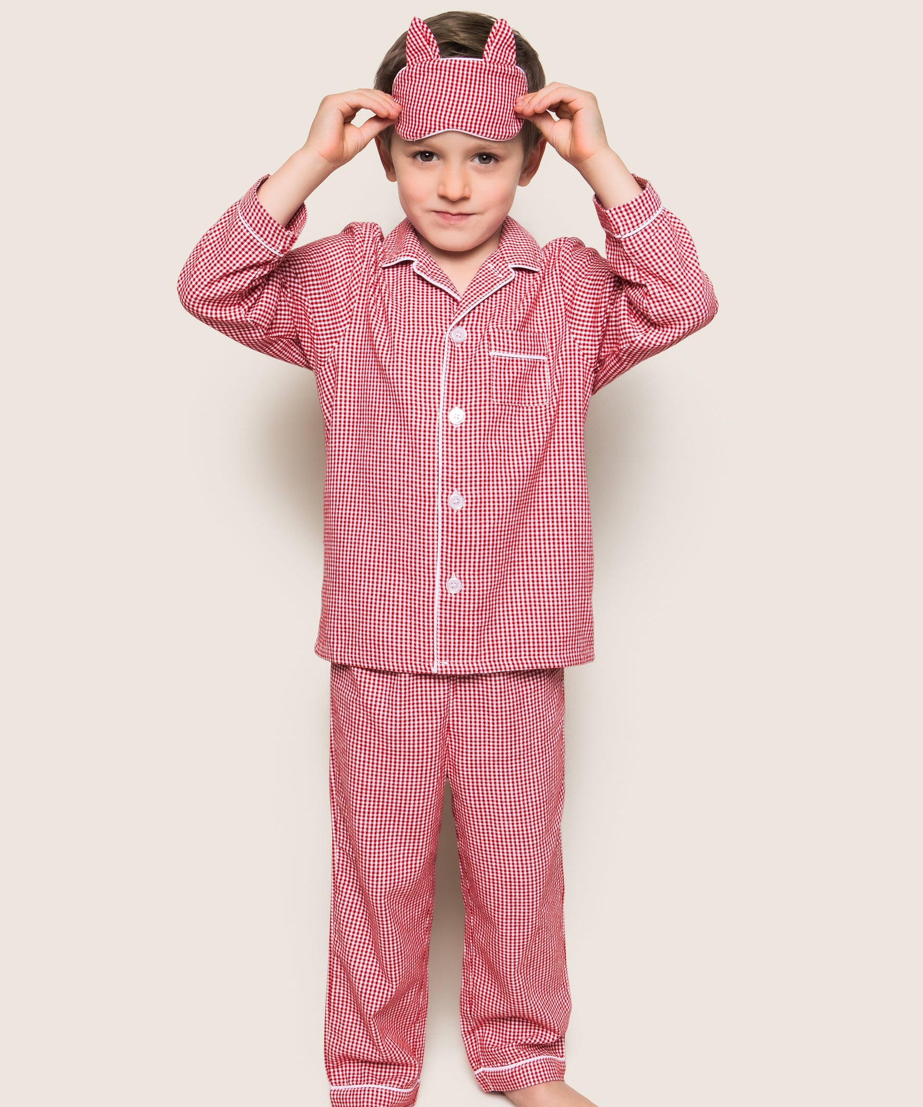 Child wearing red checkered pajama set with matching headband on a beige background