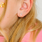 Close-up of an ear wearing a small stud earring with a strawberry design, hair partially visible.