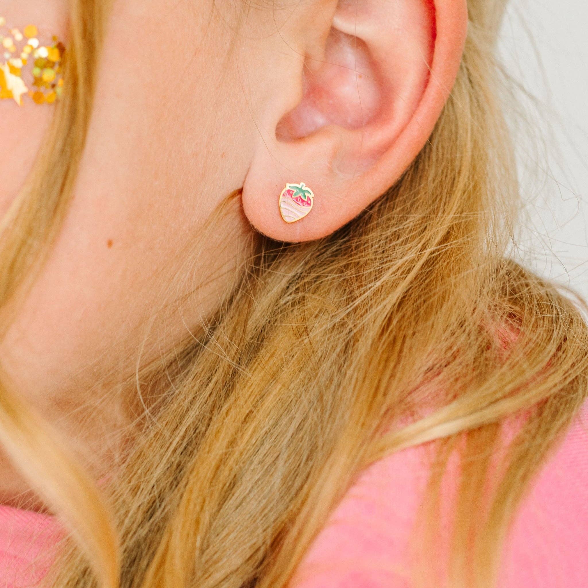Close-up of an ear wearing a small stud earring with a strawberry design, hair partially visible.