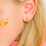 Close-up of an ear wearing a gold gumball earring with blonde hair and pink top.