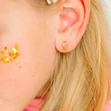 Close-up of an ear wearing a gold gumball earring with blonde hair and pink top.