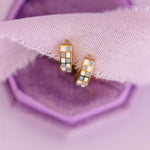 Two gold hoop earrings with a checkered purple white pattern on a purple fabric background