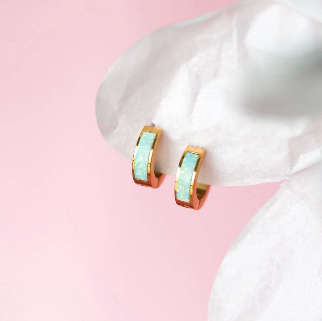 Gold hoop earrings with opal centers on a white surface with pink background