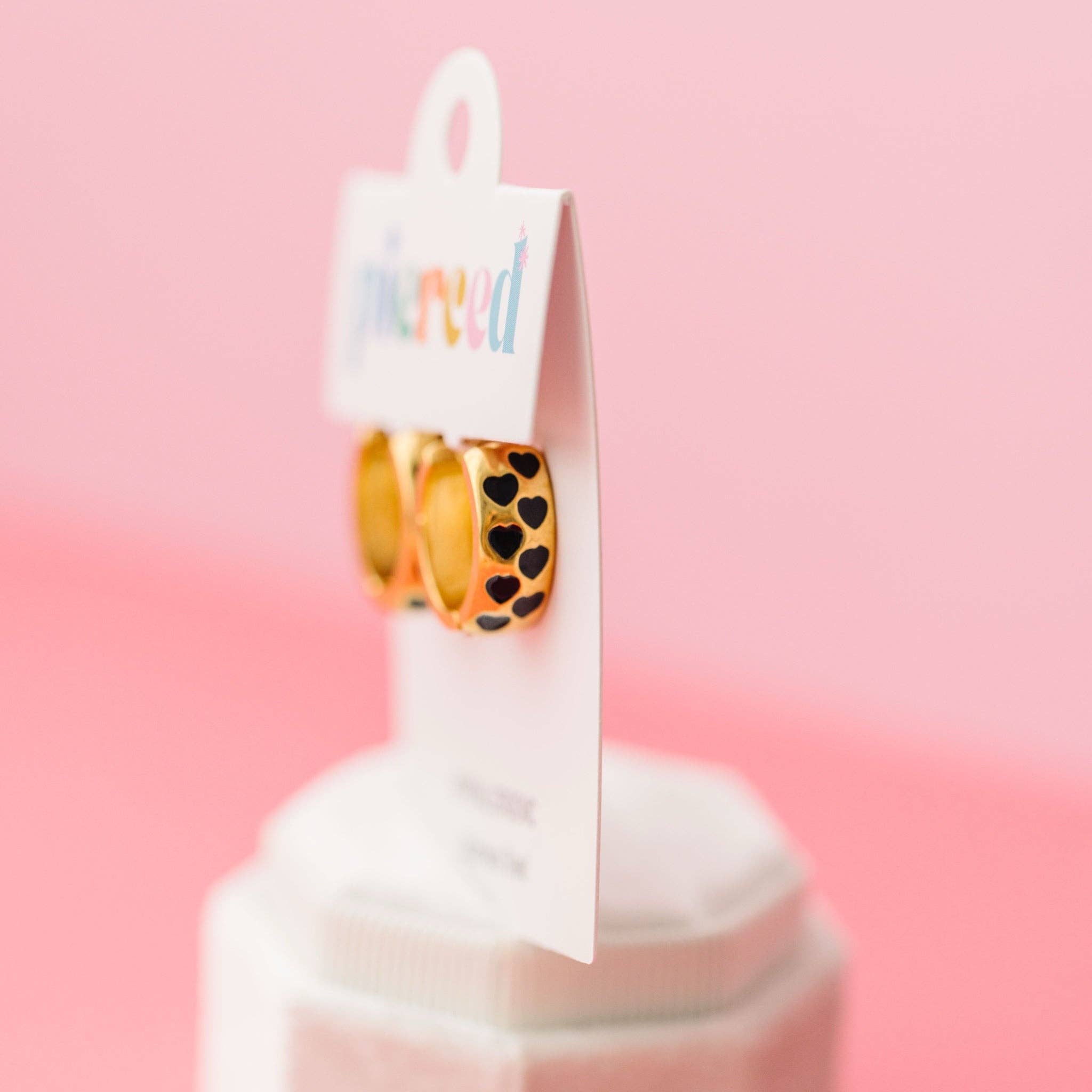 Pair of gold earrings with black heart patterns on a pink background