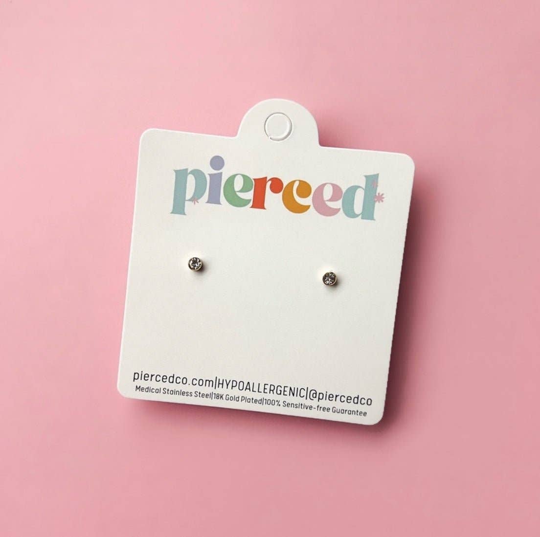 Pair of earrings on a 'pierced' branded card against a pink background