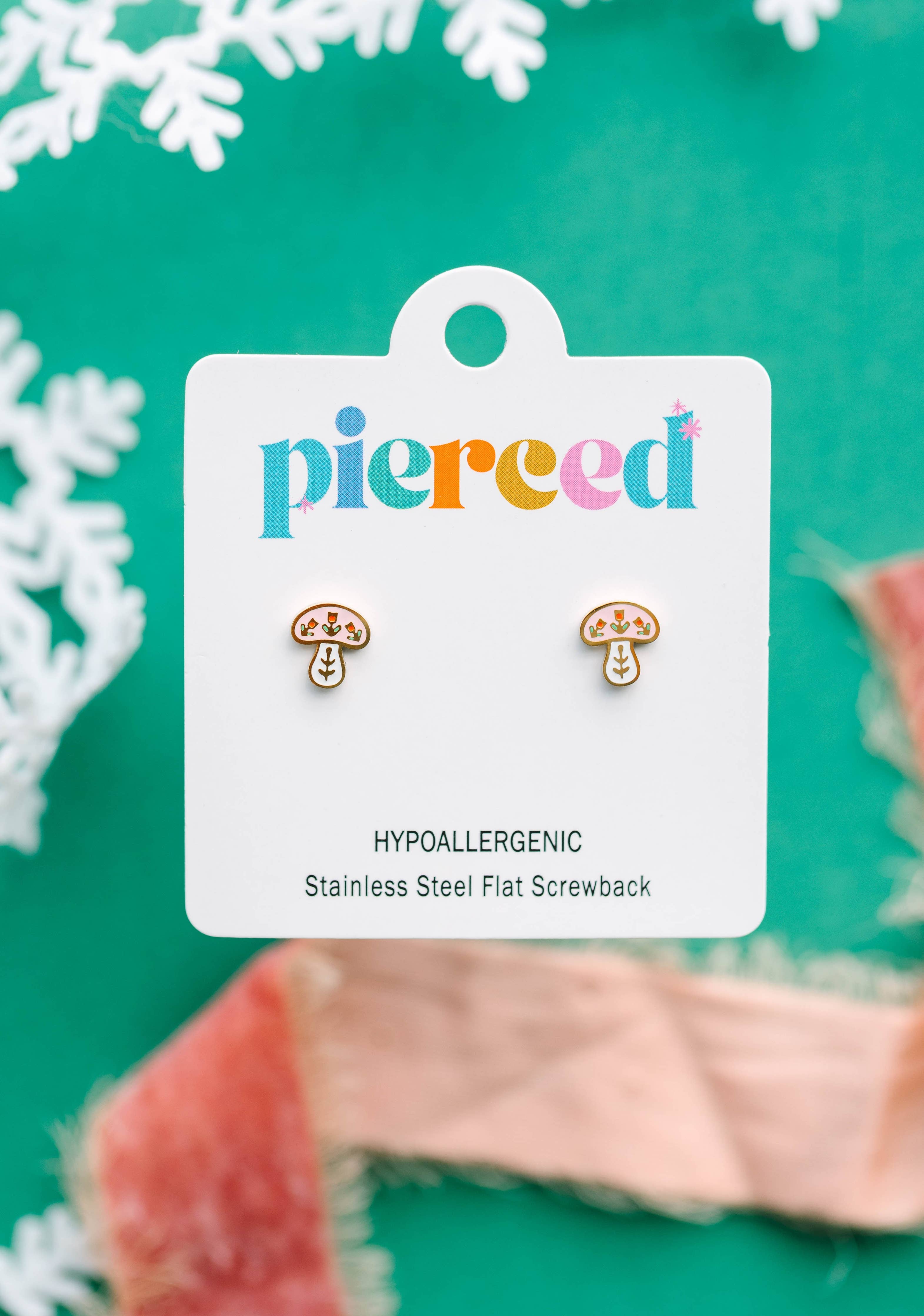 Mushroom-shaped earrings on a 'pierced' branded card with a green background