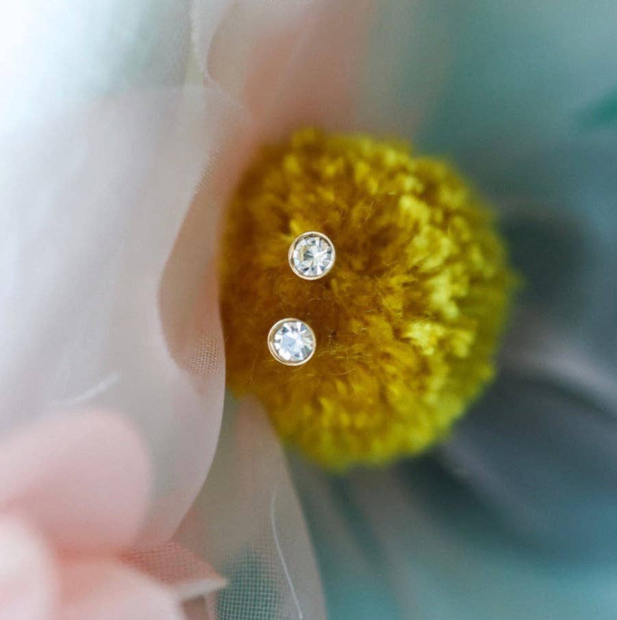 Close-up of a yellow knitted ball with two silver diamond stud earrings on a blurred background