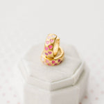Gold earrings with pink heart patterns on a white surface