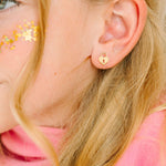 Close-up of a person wearing gold heart-lock shaped earrings with pink background