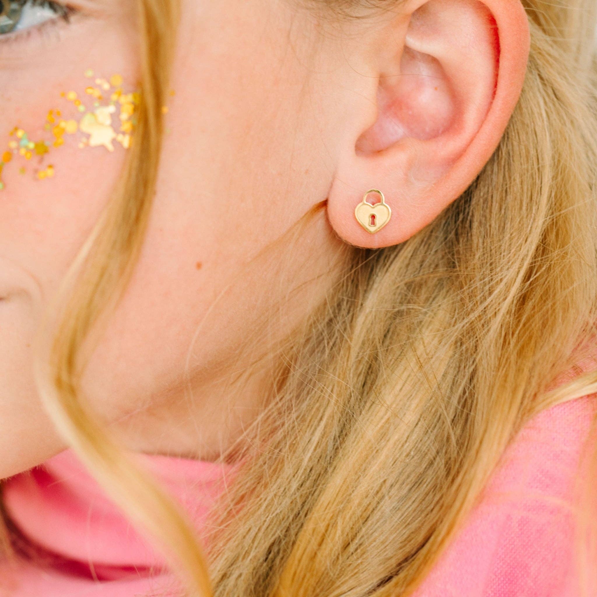 Close-up of a person wearing gold heart-lock shaped earrings with pink background