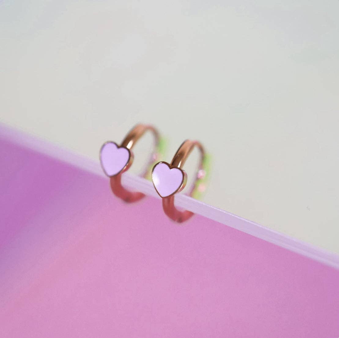 Heart-shaped huggie earrings on a pink and white gradient background