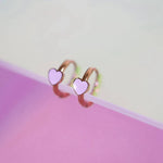 Heart-shaped huggie earrings on a pink and white gradient background